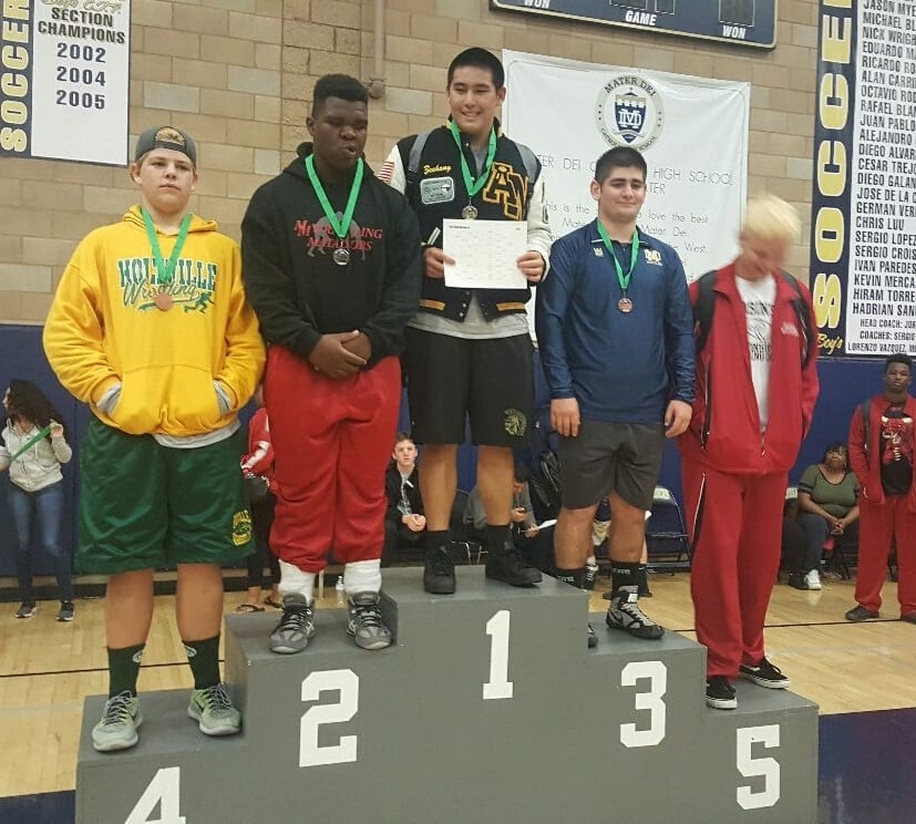 An Army and Navy Academy wrestler holds a certificate atop the awards podium at the Mater Dei wrestling tournament, flanked by second, third, and fourth-place finishers.