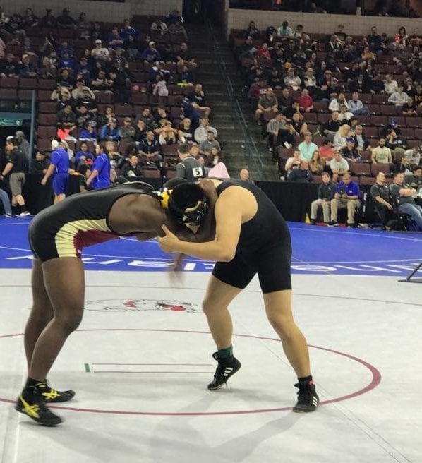 An Army and Navy Academy wrestler in black singlet grapples with an opponent on the mat at the California State Wrestling Championships.