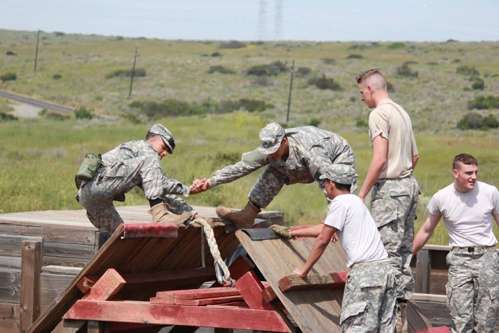 Cadets in camouflage uniforms work together to scale a wooden obstacle on a leader reaction course at Army and Navy Academy.