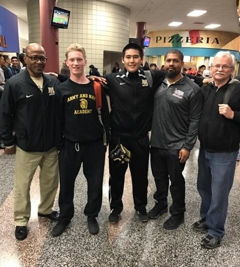 Two Army and Navy Academy wrestlers pose with three coaches inside a tournament arena at the California State Wrestling Championships.