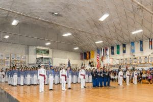 Army and Navy Academy cadets in white dress uniforms stand in formation inside the gymnasium during an academic awards ceremony.
