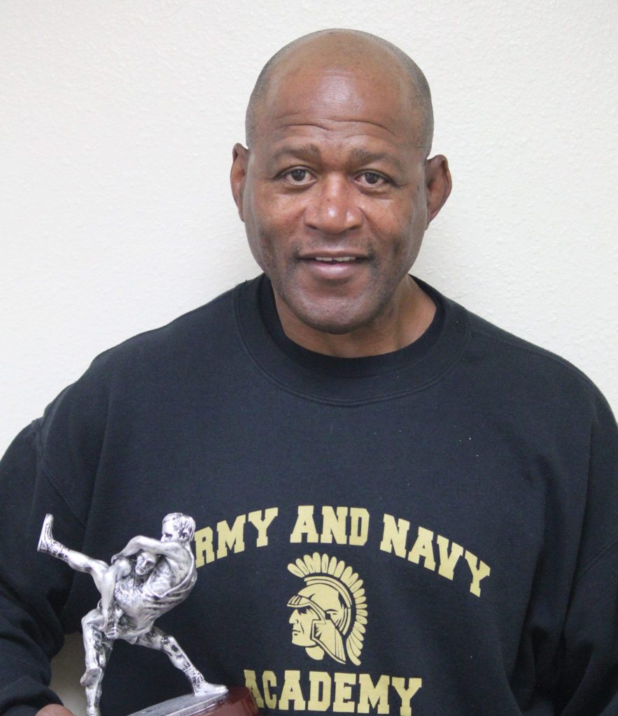 Wrestling coach Roye Oliver in an Army and Navy Academy sweatshirt holds the 2017 SD County Championships Coaches Award trophy.