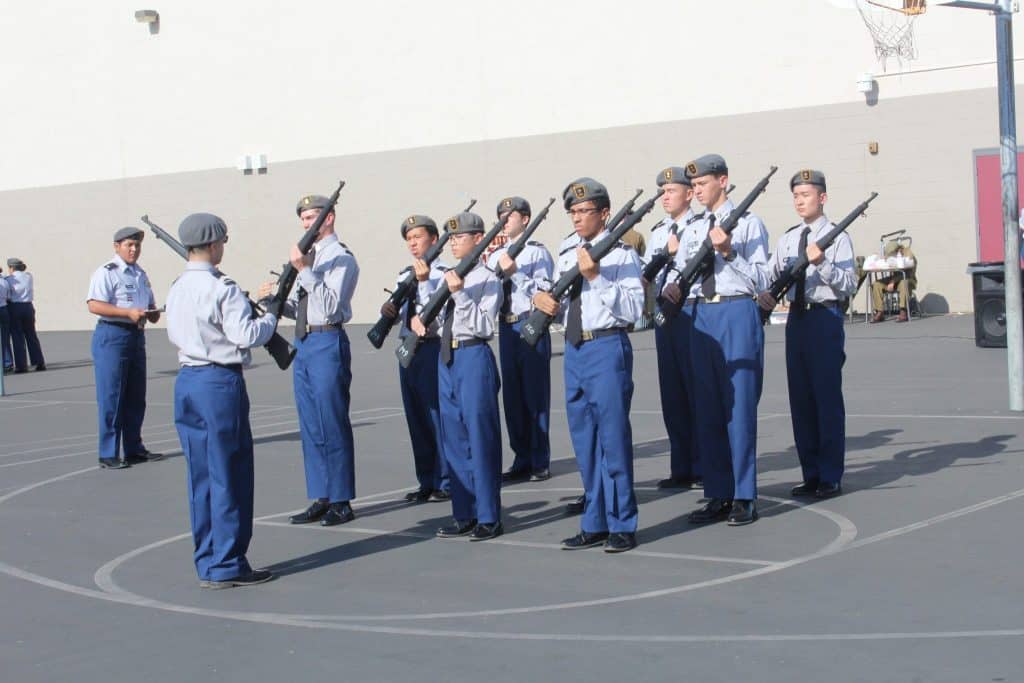Army and Navy Academy cadets in dress gray uniforms execute a rifle drill in formation during a JROTC competition.