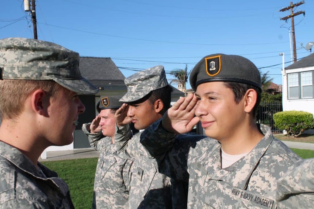 Cadets in camouflage ACUs and berets render a salute to a fellow cadet during outdoor formation practice at Army and Navy Academy.