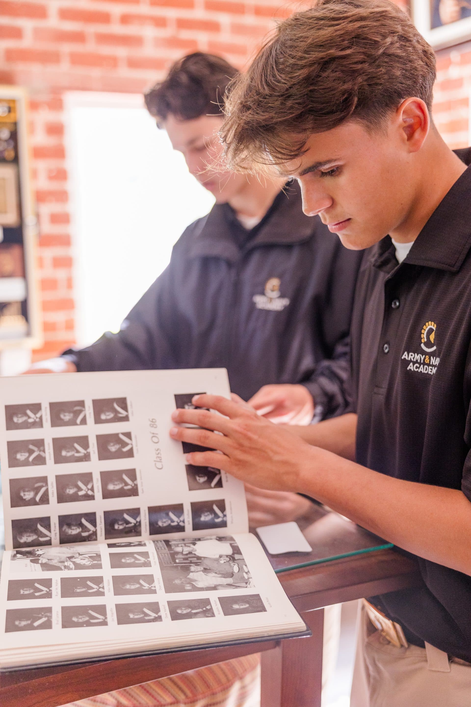 Two cadets in Army and Navy Academy polo shirts examine a historical yearbook in the alumni museum.