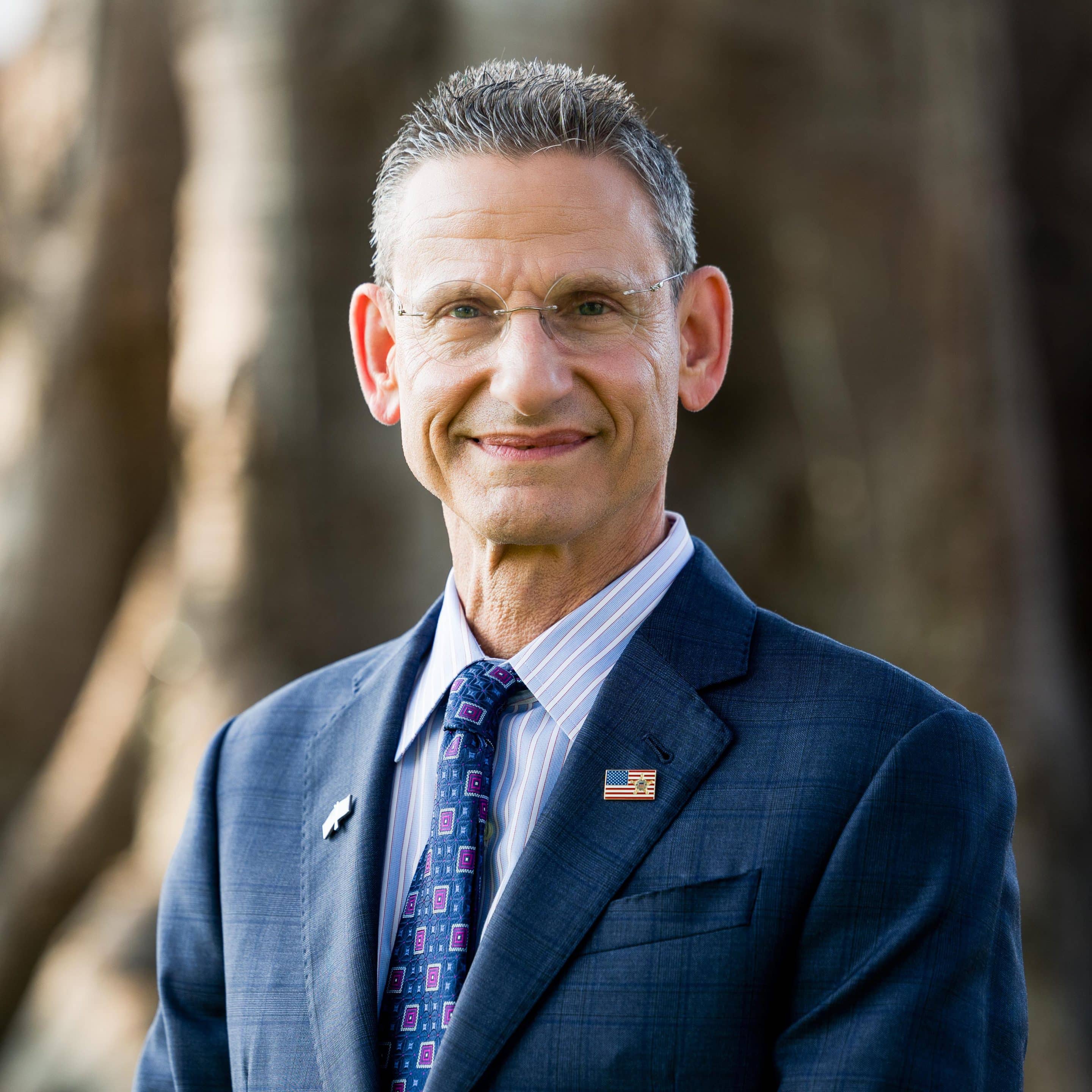 Formal portrait of Army and Navy Academy President Barry Shreiar in a blue suit with an American flag lapel pin.
