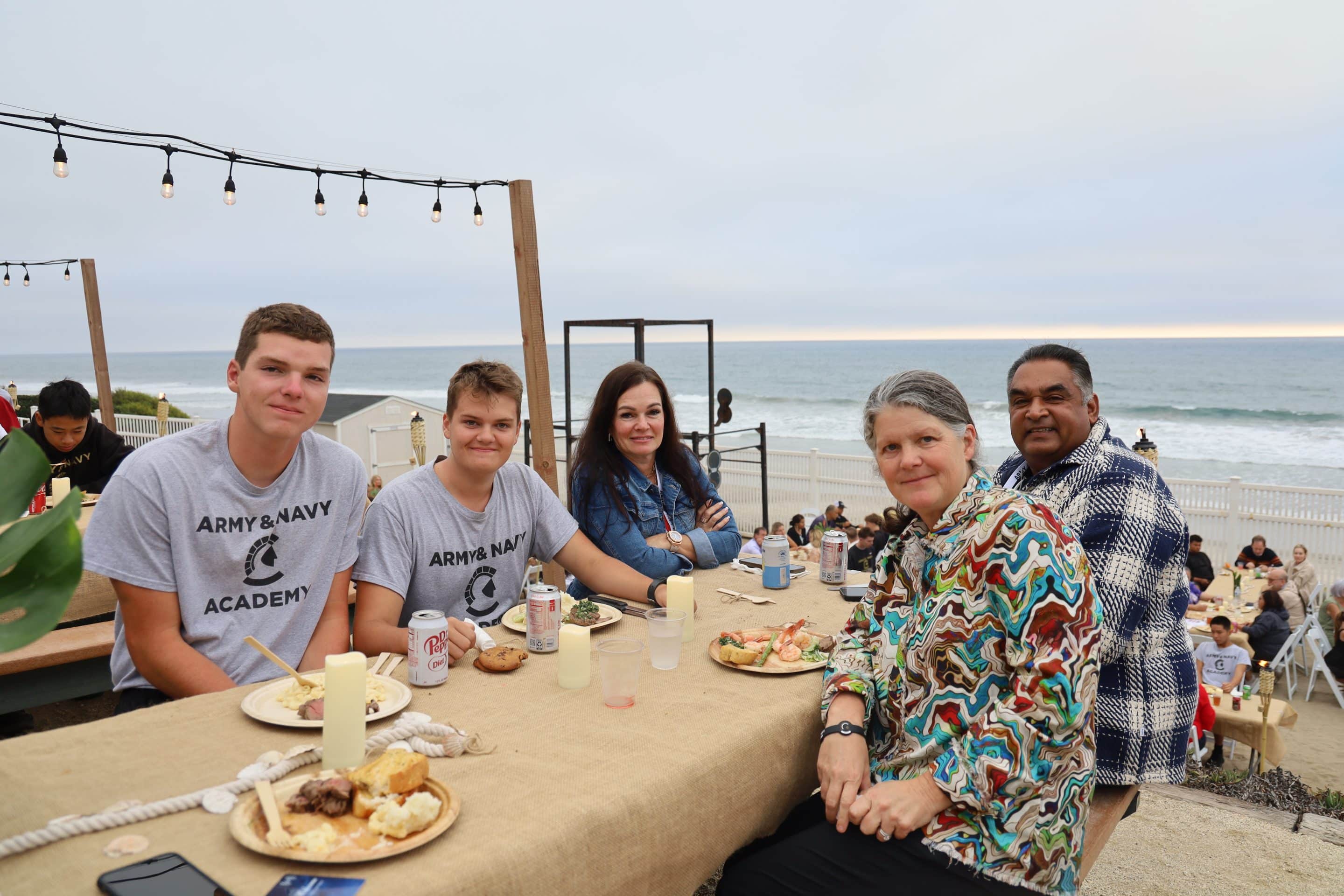 Cadets and families share a meal during an Army and Navy Academy beach event.
