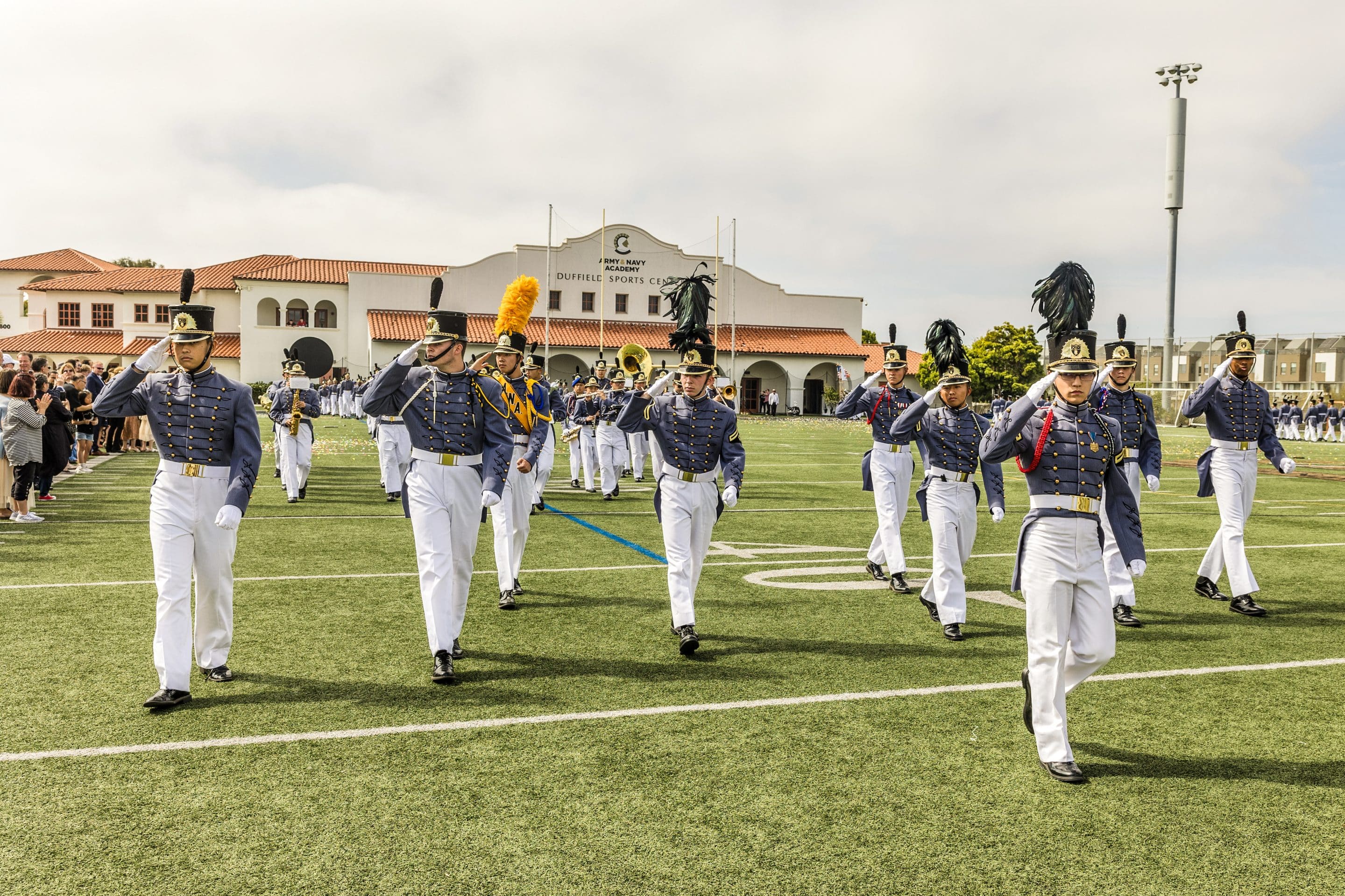 Army and Navy Academy corps of cadets in full dress uniforms and shakos marches across the football field during a formal parade.