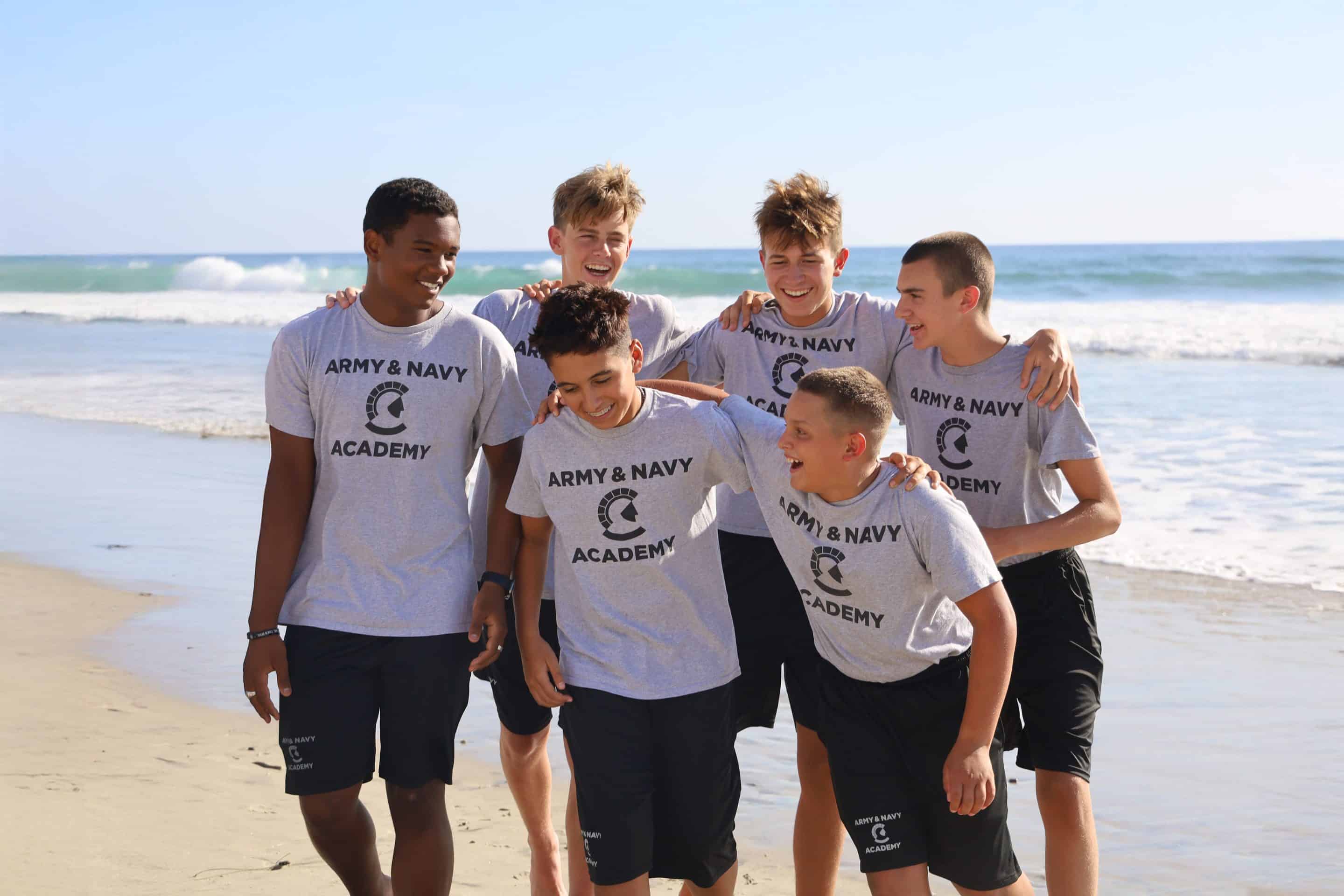 Six Army and Navy Academy cadets in grey ANA t-shirts laughing together on the beach in Carlsbad, California.