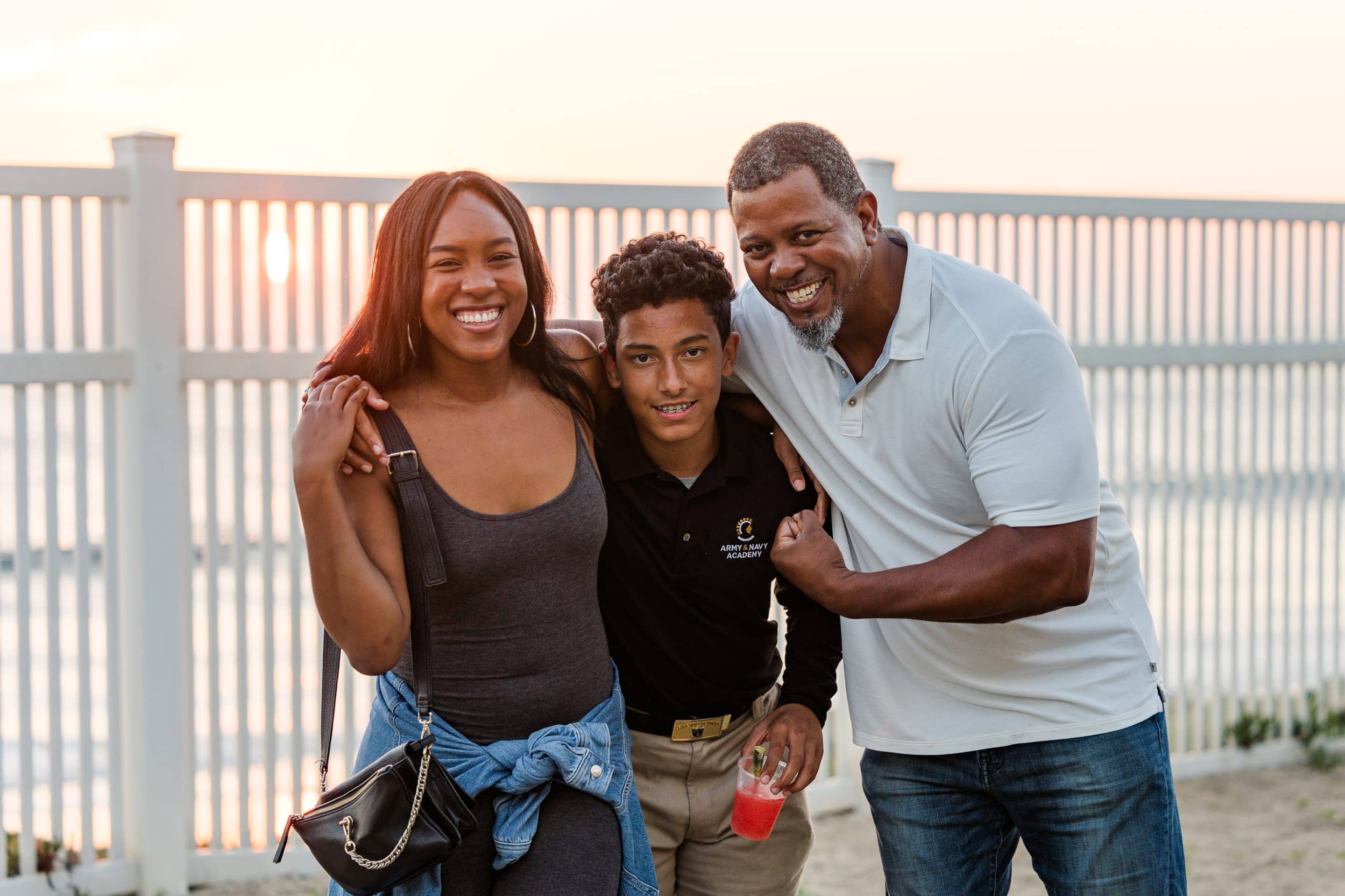A cadet and his family smile together at a sunset beachfront event at Army and Navy Academy.