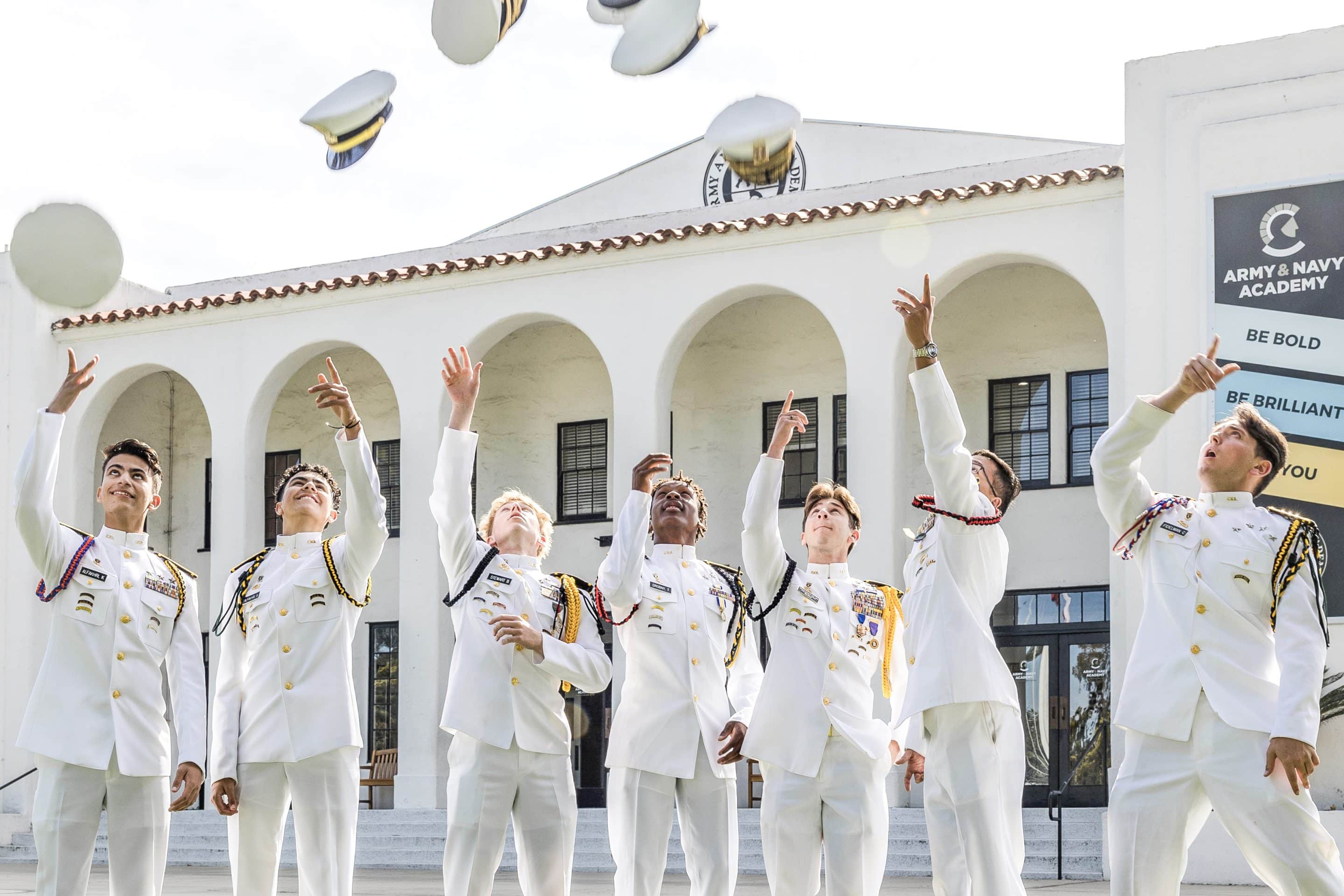 Army and Navy Academy seniors in white dress uniforms tossing their caps in celebration on the campus lawn.