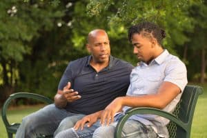 A father and his teenage son sit on a park bench having a heartfelt conversation about boarding school.