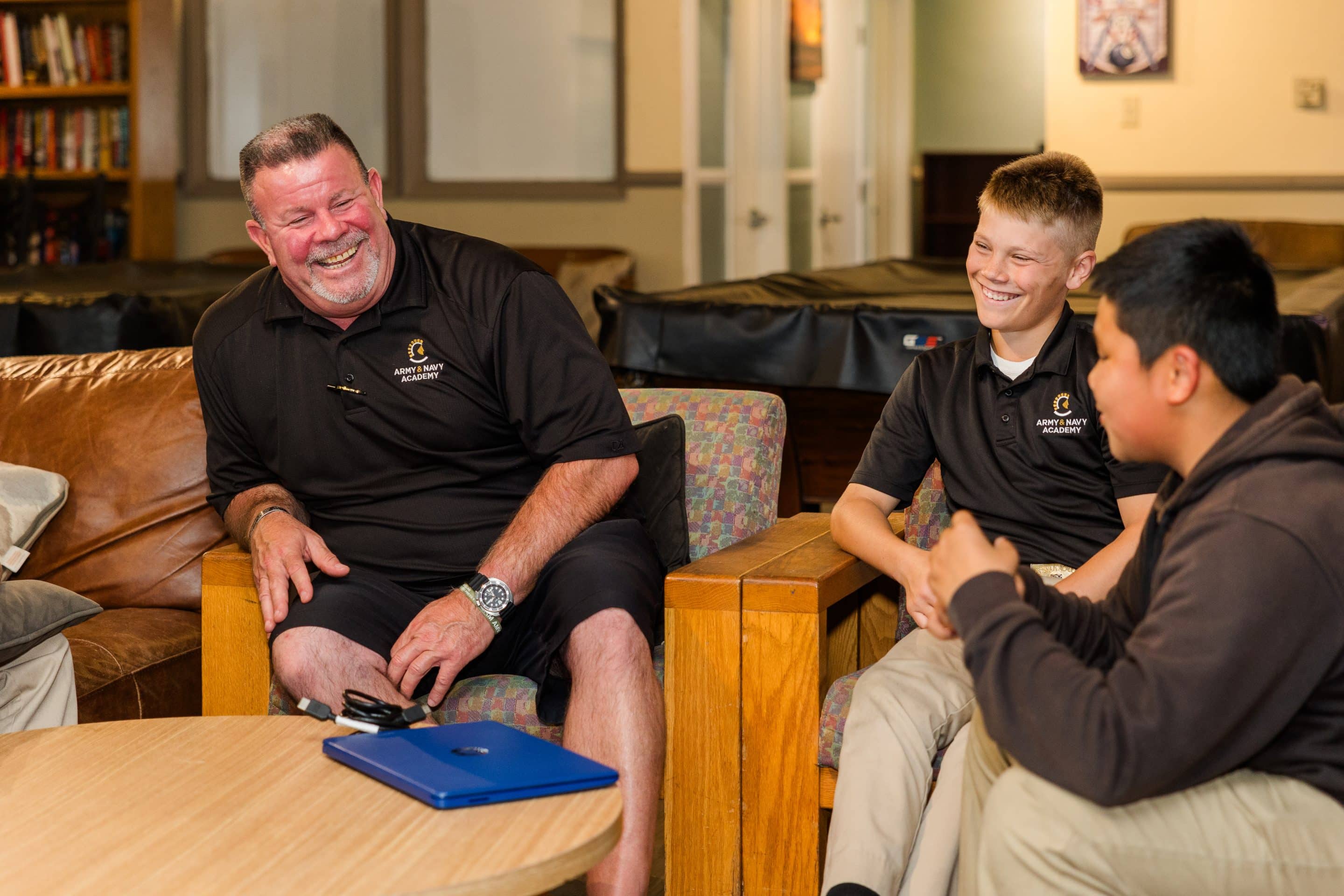 An Army and Navy Academy residential staff member laughs with two cadets in a dormitory common room.