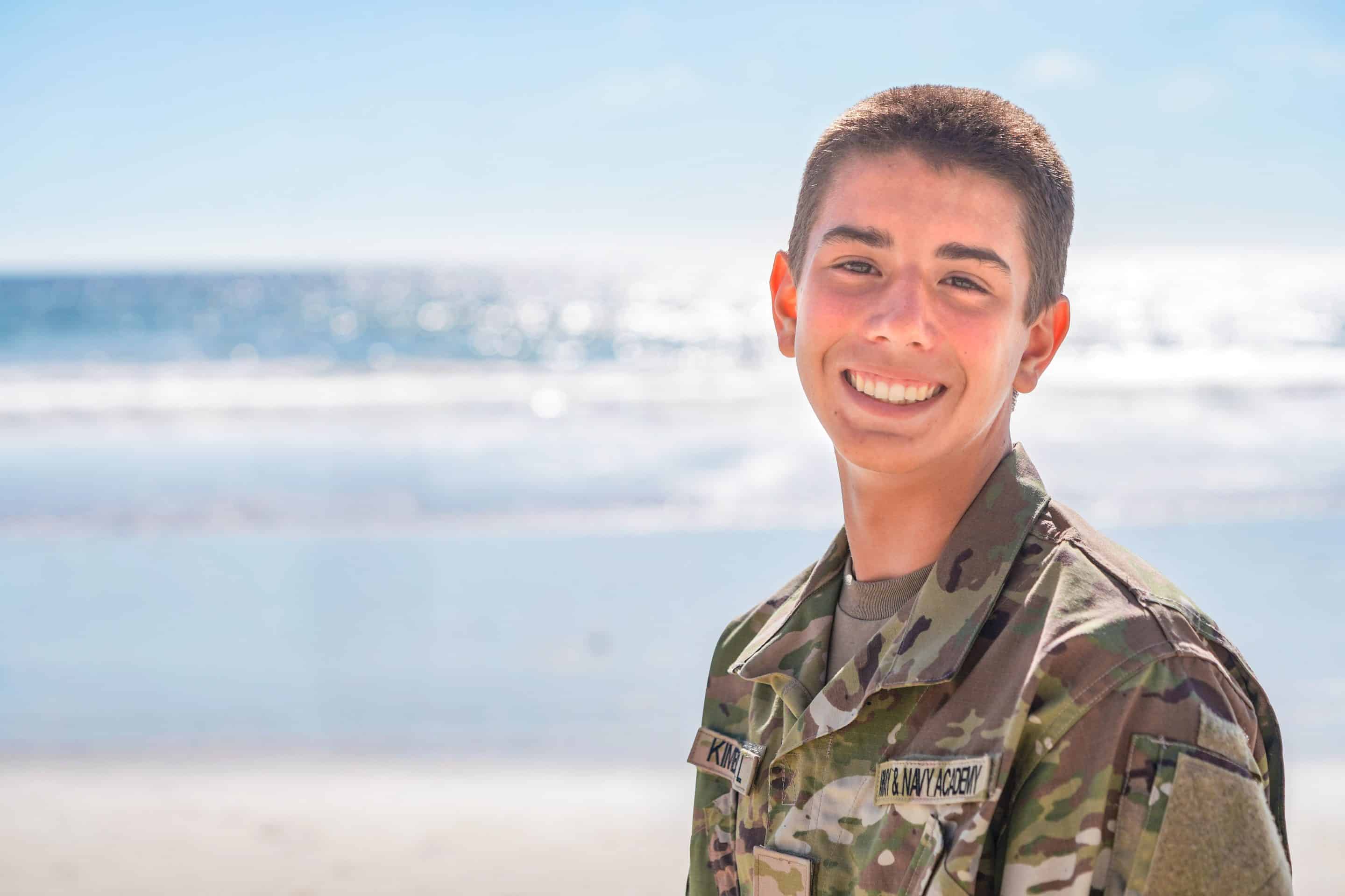 Army and Navy Academy cadet in camouflage uniform smiles on the beach on a bright sunny day.